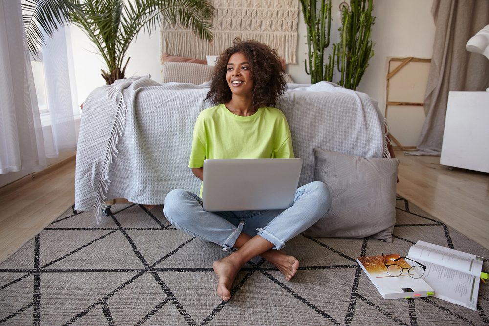 Cheerful young dark skinned woman sitting on floor using laptop and shopping online using Rakuten.png
