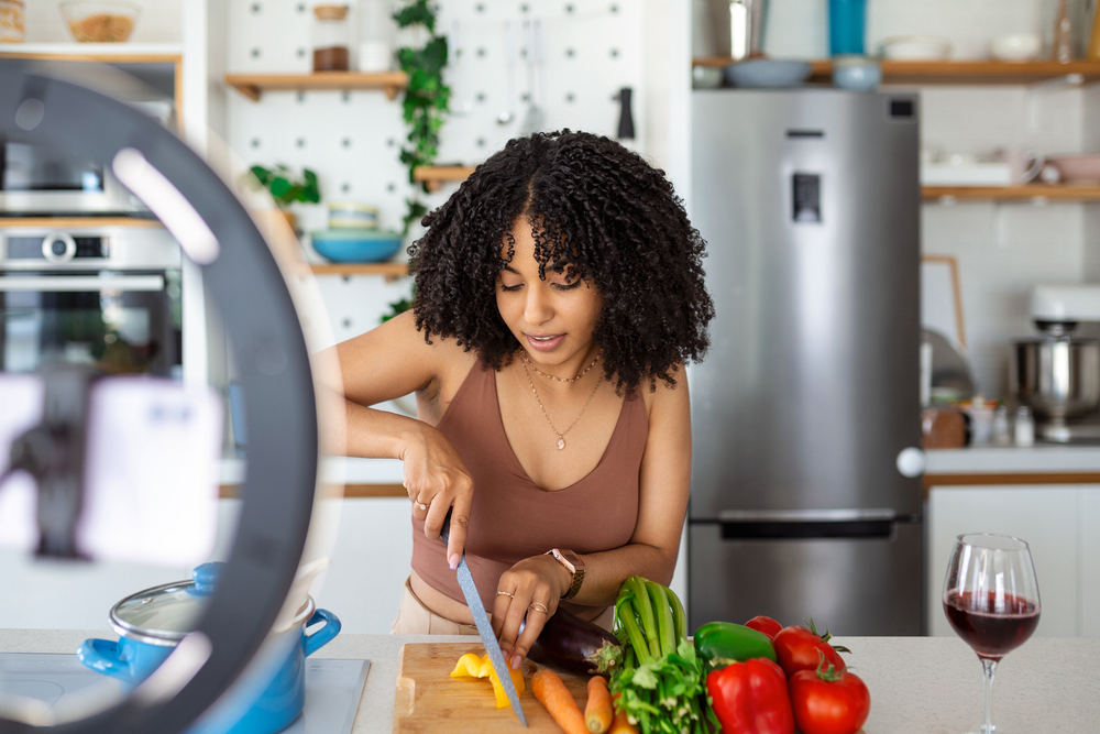 Food blogger wearing apron chopping veggies making bew recipe to sell online.png