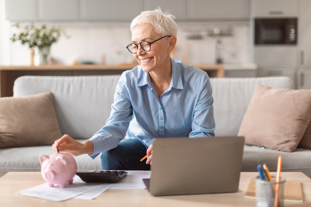 Older woman with piggy bank and laptop for the blof post Make Money Quickly as a Woman.png