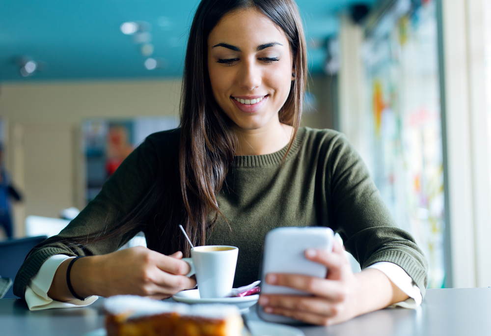 Woman with long hair drinking coffee in a cafe working her mobile phone job.png