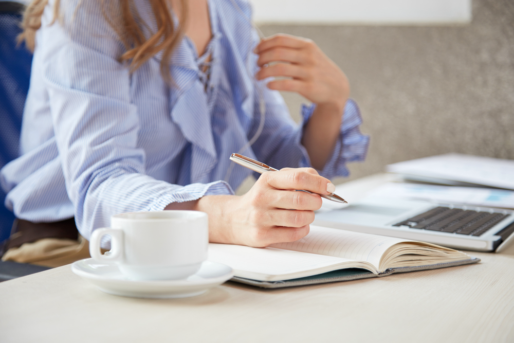 Woman writing in a note book researching how to write a cover letter on ler laptop.png