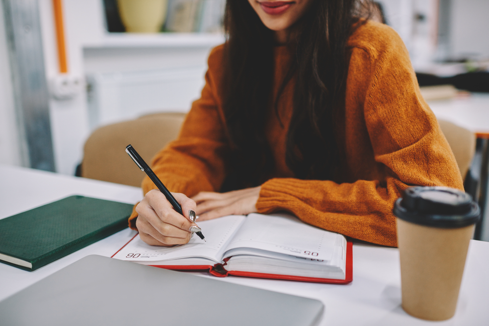 Woman writing in her notebook planning out her paid writing jobs.png