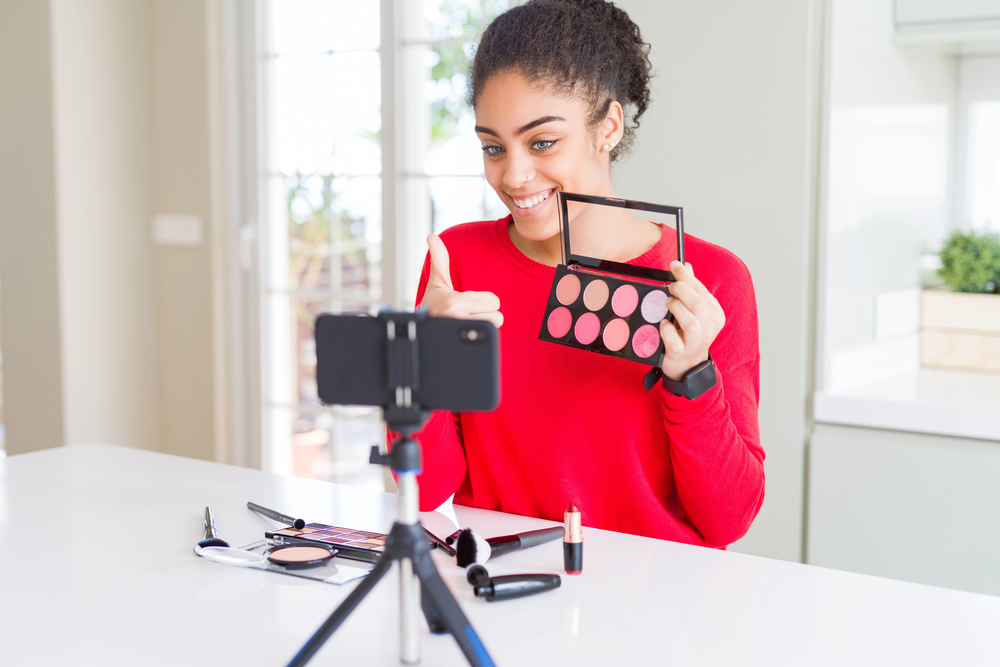 Young female Amazon Influencer filming a review video on makeup.png