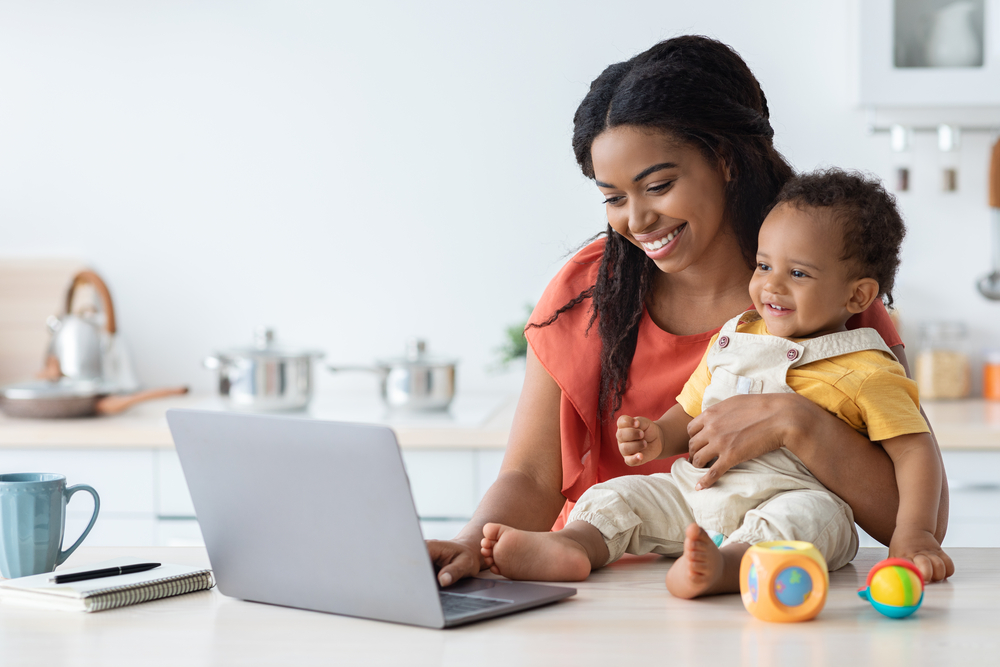 Young mom holding baby working on short tasks on her laptop.png