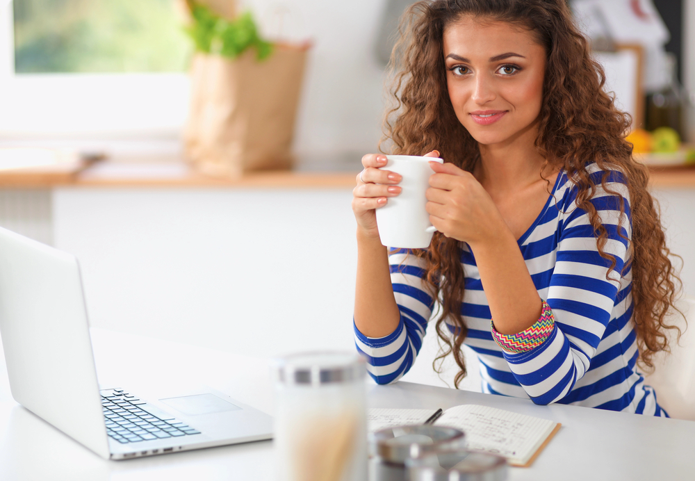 Young woman drinking coffee working on her laptop for her remote internet research job.png