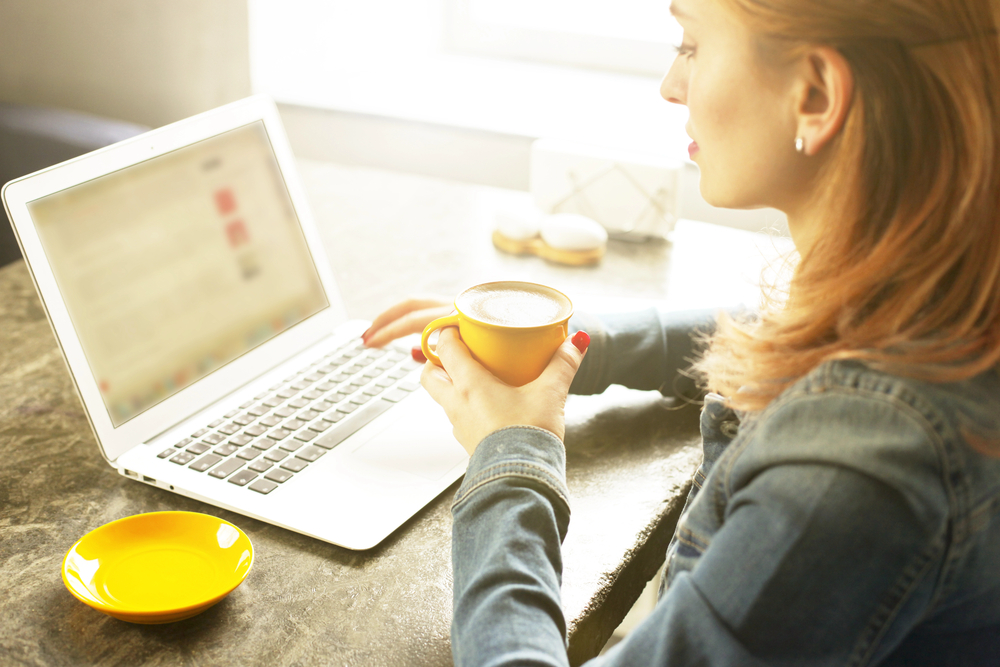 Young woman in coffee shop working on laptop trying to figure out how to get a work from home job.png