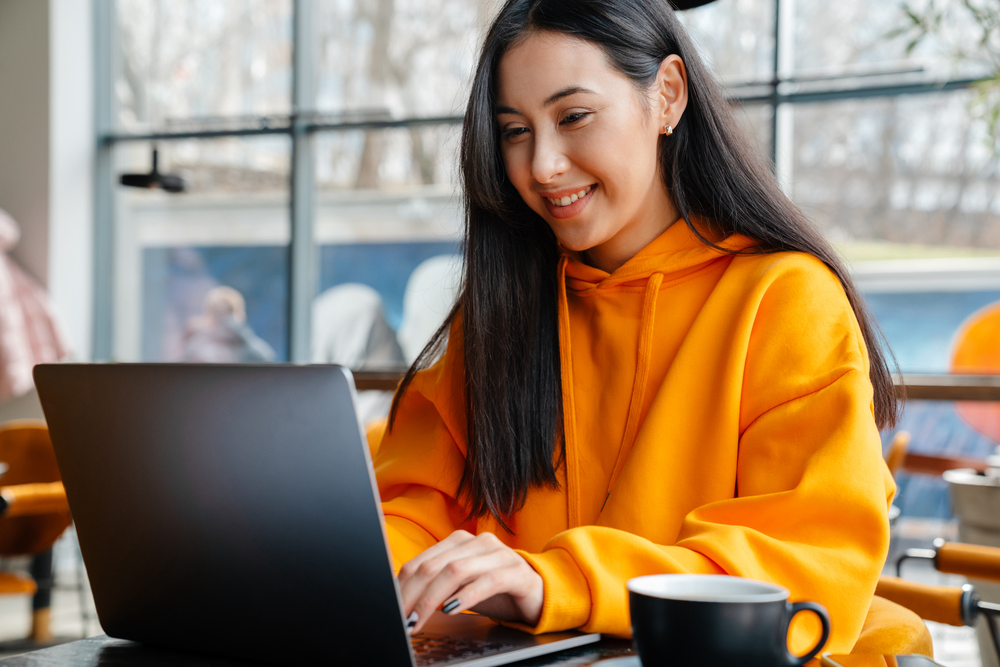 Young woman with long hair sitting in a cafe working on her laptop looking for remote facebook jobs.png