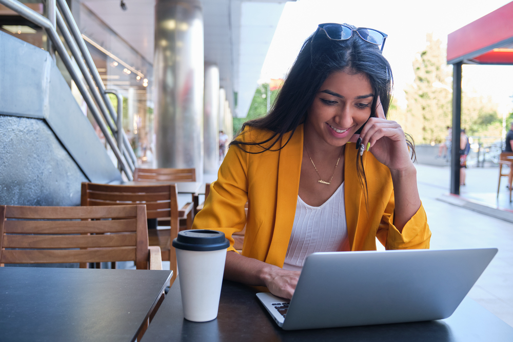 Young woman working at a cafe on her laptop for her flexible work from home jobs.png