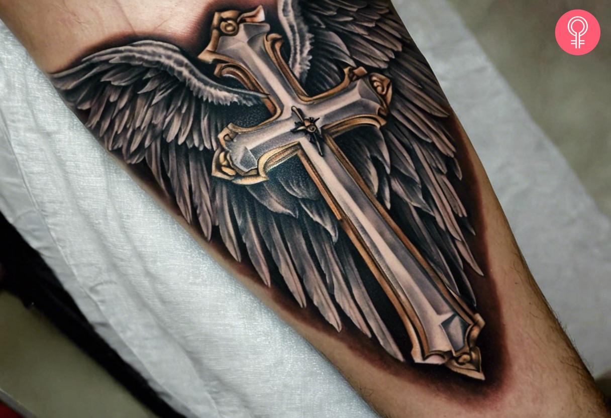 A realistic cross tattoo with wings inked on a mans forearm.jpg