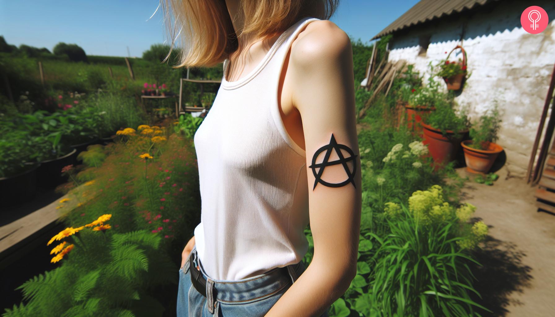 A woman with a black anarchy symbol tattoo on her upper arm.jpg