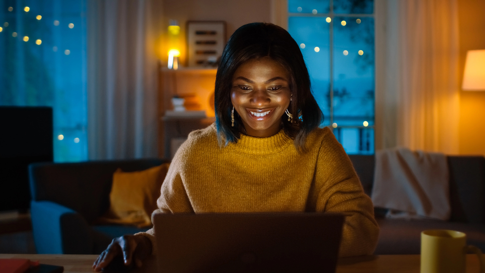 Beautiful Smiling Black Girl Working on a Laptop while Sitting at Her Desk at Home. In the Evening Creative Woman Works on a Computer at night .png