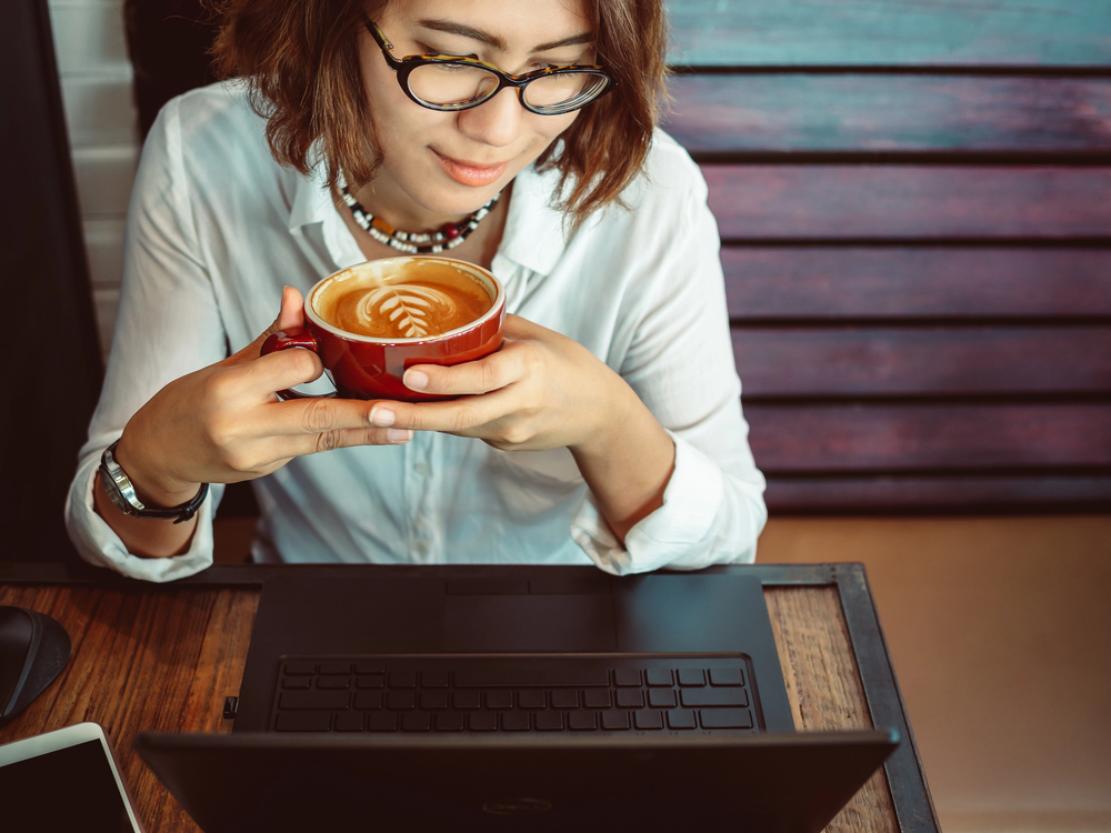 Woman at a coffee shop reading a TELUS Digital review on her laptop.png