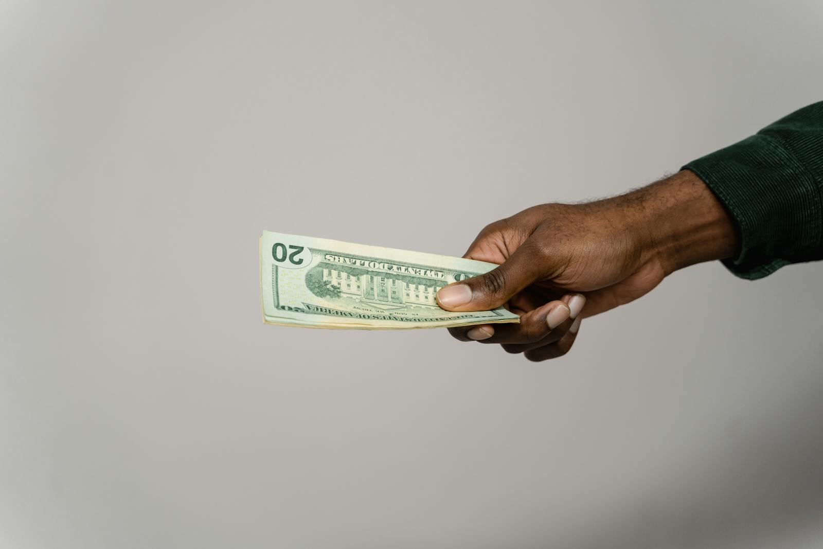 To Make 20 Dollars Fast A hand holding a twenty dollar bill against a plain gray background.